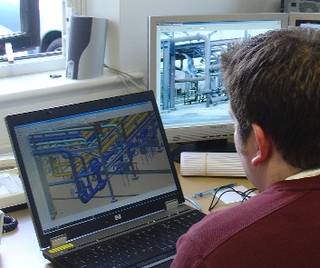 Jamie Gower bei seiner Arbeit an einem M4 PLANT-Modell einer Öl-Anlage mit dem Foto der Anlage im Hintergrund.